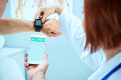 Doctor showing senior patient how to synchronize health app in smartphone and smartwatch